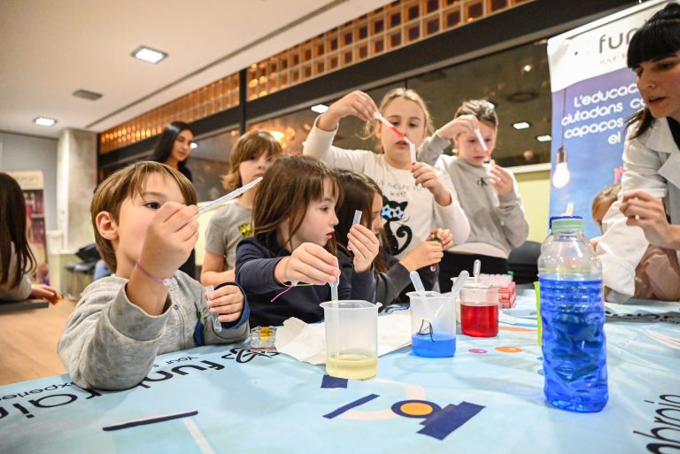 Infants fent experiments científics amb pipetes i líquids de colors en una taula de laboratori.